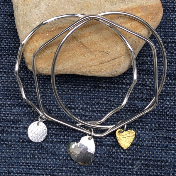 Silver charm bangles on a blue and stone background