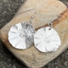 silver dangly earrings with hammered texture and flower stamp on a stone background