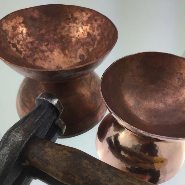 Copper bowls with hammer on mirrored surface