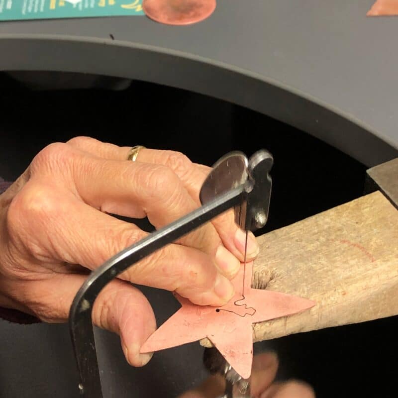Hands saw piercing copper star on benchpeg