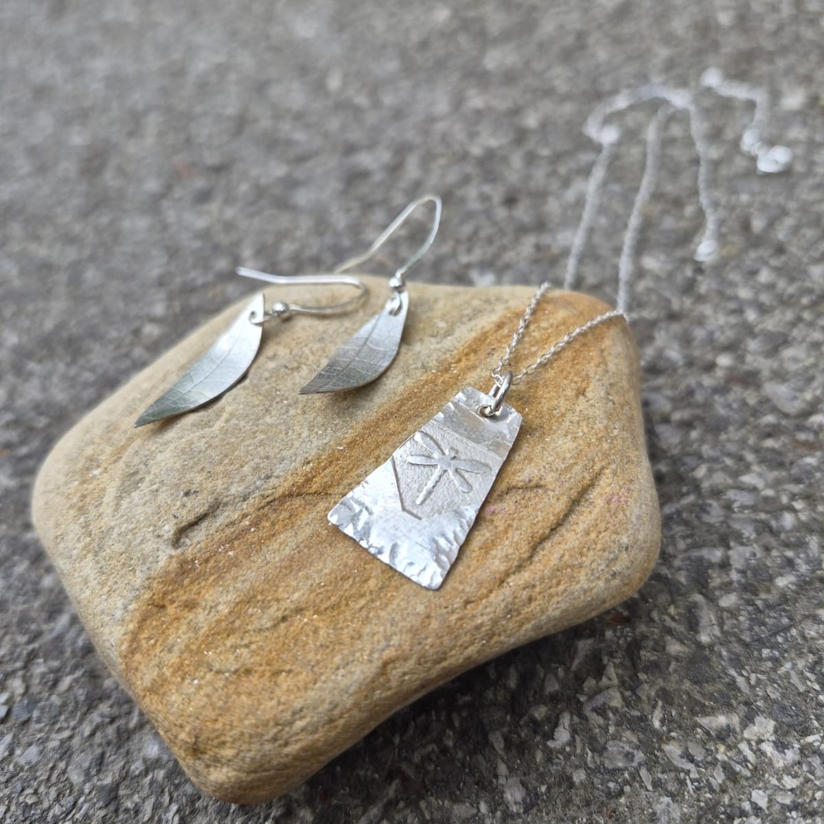 Silver pendant and earrings on stone background